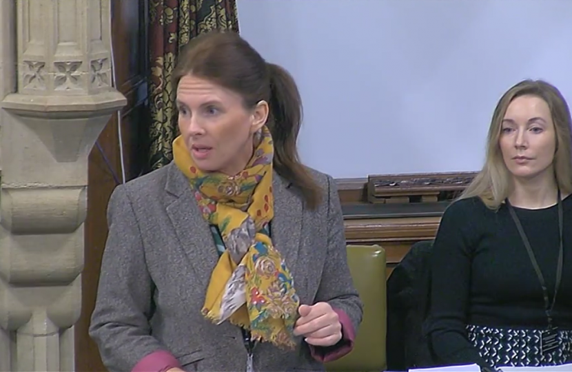 Trudy at the debate, speaking in a grey jacket with a yellow floral scarf and her hair in a ponytail